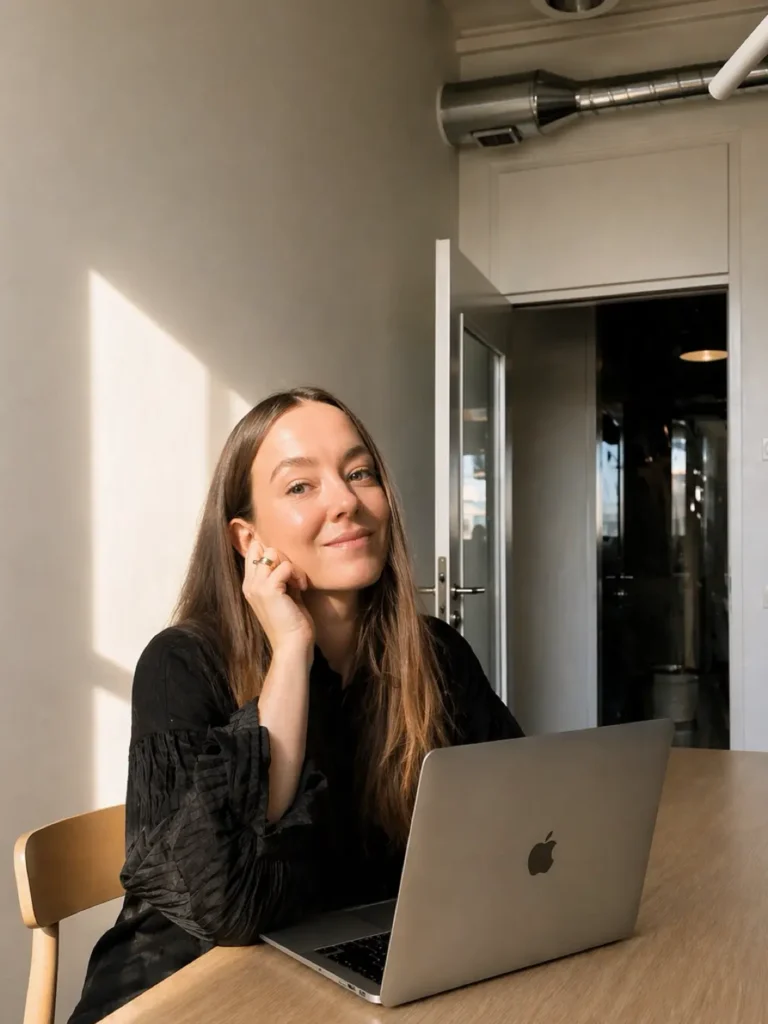 Bild på webbdesigner som jobbar med laptop framför sig och ler in i kameran.